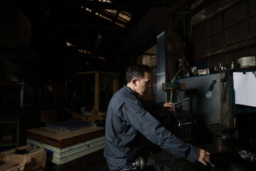 Fototapeta na wymiar Metalworker in gray work clothes and a lathe in a small to medium-sized small business town factory. Conceptual images of the essence of manufacturing and technical succession.