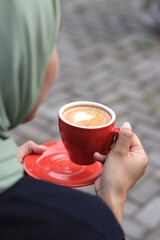 a girl hand holding a glass of hot cafe latte with latte art in the morning