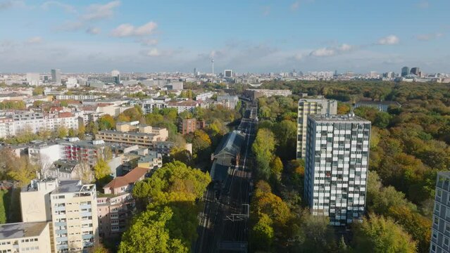 Backwards fly above multitrack railway line in city. Panoramic view of buildings and large park in metropolis. Berlin, Germany