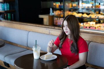 A woman cuts a white coconut cake and drinks a milkshake alone.