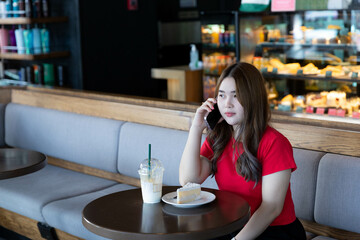 A woman talking on phone with friend while eating cake and drink in restaurant