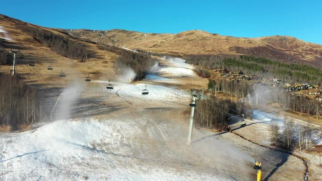 Snow production in alpine resort destination Myrkdalen Norway - Ascending aerial showing recently started snow cannons blowing out artificial snow during start of season
