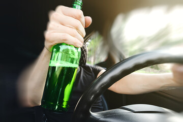 Close-up of a bottle of Alcohol in the driver hand at the wheel of car. Alcohol driving concept.
