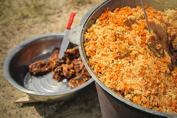 Traditional oriental pilaf in big cauldron on a sunny day outdoor. Real central asian pilaf in the steppe.