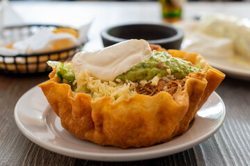 A crisp Mexican taco bowl made with a round baked tortilla shell filled with beans, corn, beef,...