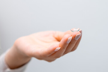 Close up woman hand with contact lens on the grey background