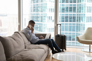 Busy young millennial travelling business man using digital gadgets for communication in hotel...
