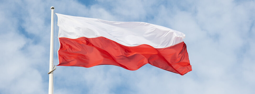 Flag of Poland waving at wind against beautiful blue sky. Polish flag White and red flutters on blue sky. National flag of Poland flapping on flagpole with sky behind
