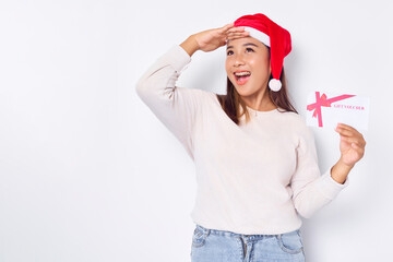 Excited young Asian woman 20s in a Santa Claus hat holding a gift certificate coupon voucher card,...