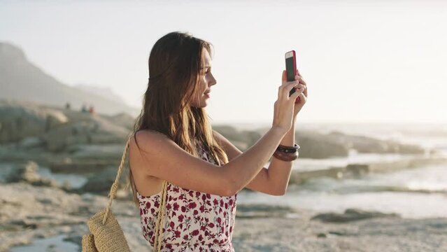 Woman, phone and beach to photograph, on travel holiday with ocean view to post or share on social media. Sightseeing female using technology to record sunset over a sea in a tourism destination