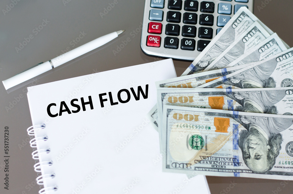 Aufkleber cash flow text on a notepad on a table next to a pen, calculator and dollar bills on the table