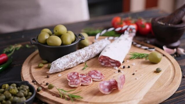 Sliced circles of traditional fuet sausage falling down on wooden cutting board at domestic kitchen
