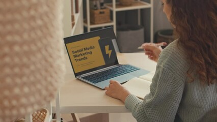 Young female marketing specialist working with smm trends from home, analyzing slide presentation on laptop