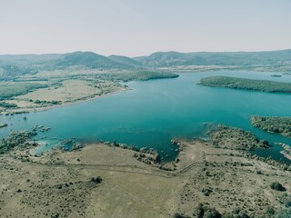 Aerial view on mountain lake. Drone over water reservoir at mountain valley covered with green spring forest. Beautiful view from above on smooth blue surface of mountain lake among highlands. Nobody
