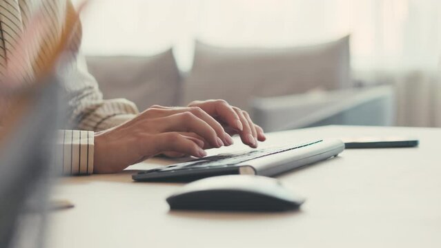 Closeup of unrecognizable female hands typing on wireless keyboard during work on computer in office or at home