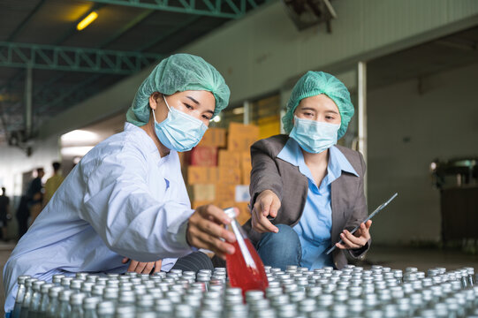 Asian Inspector Supervisor Woman With Assistant Employee Wearing In Sterile Suit Checking For Stock Product Of Fruit Beverage Packaging In Warehouse At Processing Plant