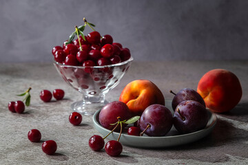 Cherry in a vase, peach and plum on a plate on a gray table
