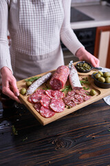 Woman holding wooden cutting board with Traditional Spanish fuet salami sausage at domestic kitchen
