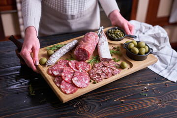 Woman holding wooden cutting board with Traditional Spanish fuet salami sausage at domestic kitchen