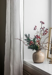 Christmas bouquet with branches of spruce, cranberries in a ceramic vase on the windowsill