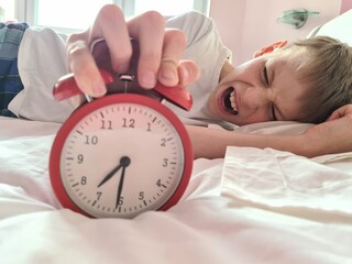 Stressed tired boy sleeping in bed with an alarm clock