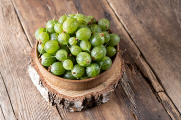 Green gooseberries in a wooden bowl. Harvest berries on a wooden table. Gooseberry summer vitamin food.
