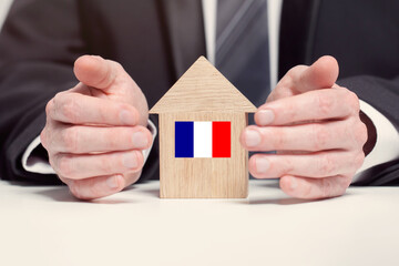 Businessman hand holding wooden home model with French flag. insurance and property concepts