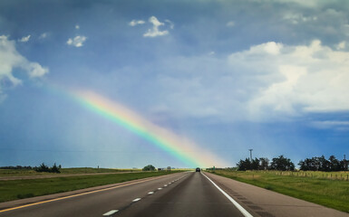 View of flat Midwestern highway after rain with rainbow on horizon