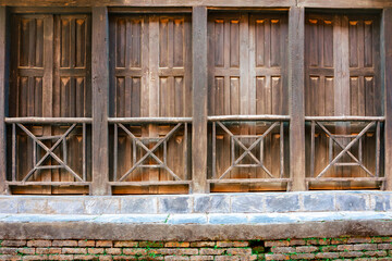 Antique, traditional wooden facade in a small village in Nepal. In the foreground is a small brick wall.