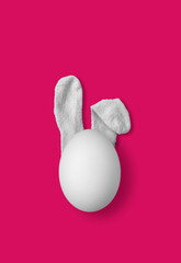 Bunny rabbit ears made of white fluffy socks with white egg on bright pink background. Easter minimal concept. Flat lay - 551752017