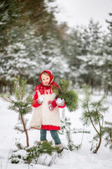 girl with branches of a fir tree in the winter forest . In the hands of a candy lollipop. She's wearing a red coat and a Russian headscarf