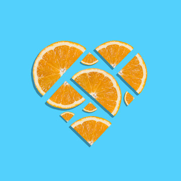 Juicy fresh orange slices forming heart shape on bright blue background. Minimal summer concept. Top view