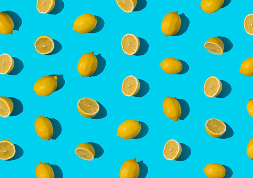 Summer pattern made with fresh cut and whole yellow lemon on bright light blue background. Minimal background summer concept on with harsh light and sharp shadow