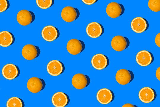 Summer flat lay pattern made with fresh whole orange fruit and slices on vibrant blue background. Minimal sunlight concept with sharp shadows