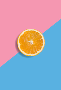 Minimalistic summer fruit tropical composition. Half of juicy fresh orange on light pastel pink and blue background. Citrus fruit refreshment. Vitamins, fresh healthy food concept. Copy space
