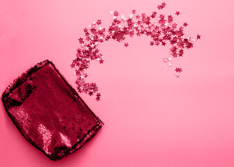 Bright violet female cosmetics bag from two-sided sequins multicolor stars confetti on pink background. Holiday concept.