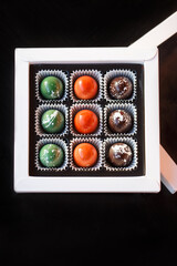 Set of different handmade chocolates in a white paper box on a black background. Holiday concept. Close up. Top view