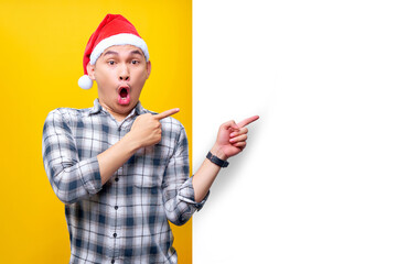 excited and surprised young Asian man in hat Christmas, standing and pointing his finger out the...