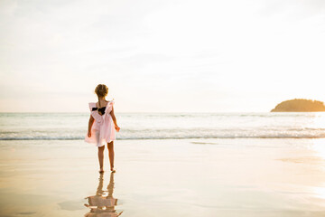 Fototapeta na wymiar Happy little caucasian girl five years old walking on the tropical beach on sunset