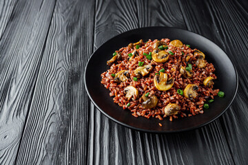 delicious red rice with mushrooms on a black wooden rustic background
