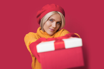 Beautiful caucasian woman wishing happy holidays, giving you gift isolated over red background. Xmas holiday background. Holiday present. Party, fashion