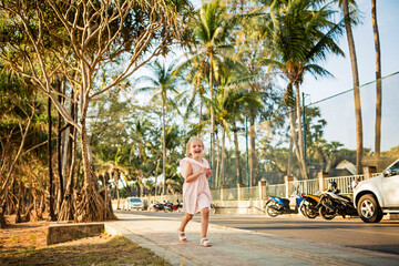 Fototapeta na wymiar Happy little caucasian girl five years old walking on the city road on sunset at summer evening