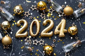The golden figures 2024 made of candles on a black stone slate background are decorated with a...