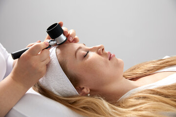 Woman gets professional skin exam at doctor's office. Dermatologist or cosmetology specialist uses...