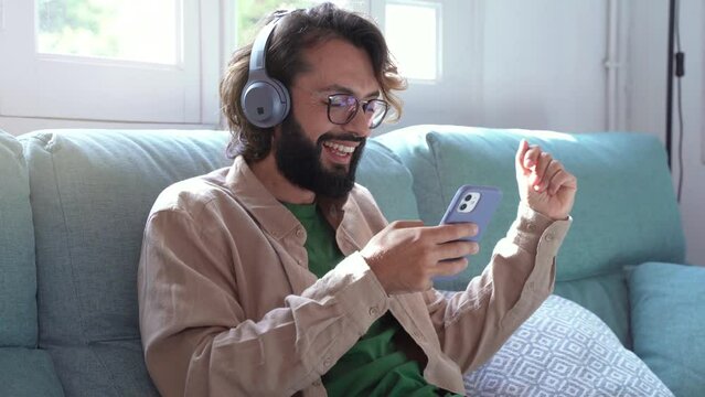 Joyful Man with headphones chilling listening to music sit on sofa, happy relaxed millennial guy