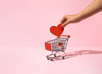 Female hand putting red paper heart in shopping cart. Minimal love or Valentine concept.