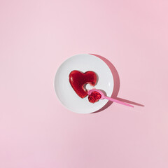 Red jelly heart scooped with plastic spoon on white plate. Love or Valentines minimal concept.