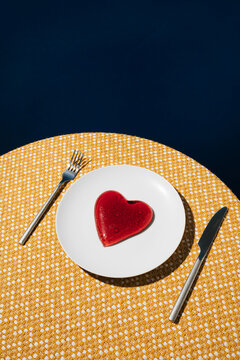 Red jelly heart on white plate and yellow table cloth with dark blue background. Love or Valentines minimal concept.