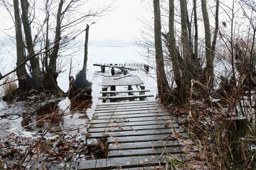 Destroyed old wooden pier among trees by lake in slightly winter scenery