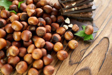Hazelnuts in shells scattered on a wooden background with pieces of chocolate. The concept is ingredients for a chocolate paste recipe.
